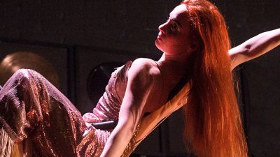 A woman with long red hair is performing an acrobatic dance using an aerial hoop