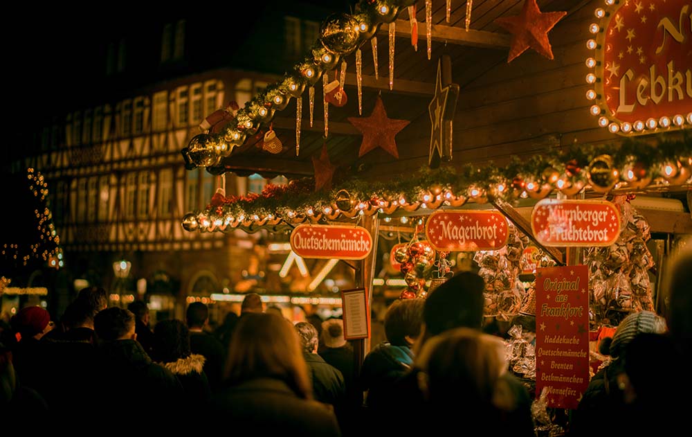 A photo shows German Christmas Markets lit up at night with a big crowd of people. 