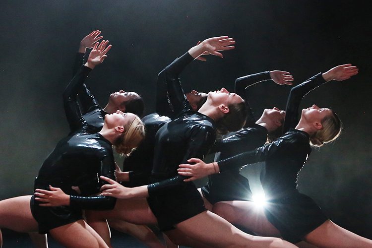 The ensemble of 'Emergence 19/20' performing on stage in black leotards