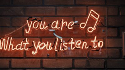 Photo of orange neon sign on a wall saying "You are, what you listen to"