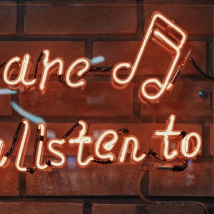 Photo of orange neon sign on a wall saying "You are, what you listen to"