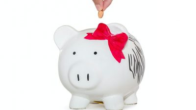 Photo of a hand putting a coin into a white piggy bank
