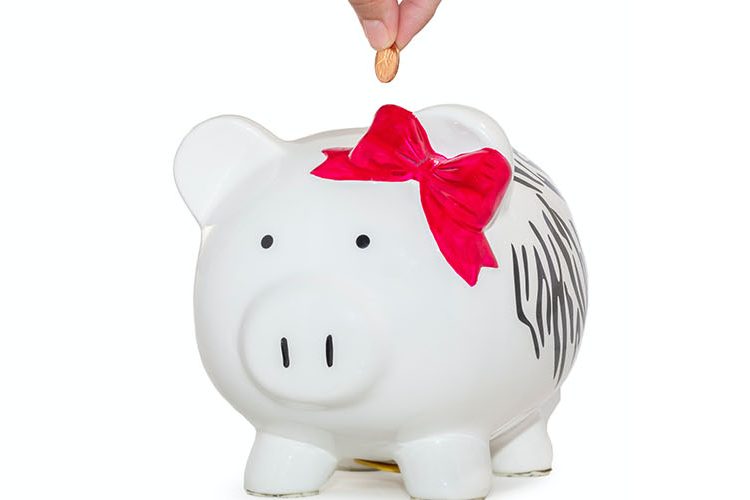 Photo of a hand putting a coin into a white piggy bank
