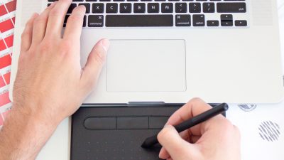 Photo of left handing typing on a macbook and right hand drawing using a digital pen