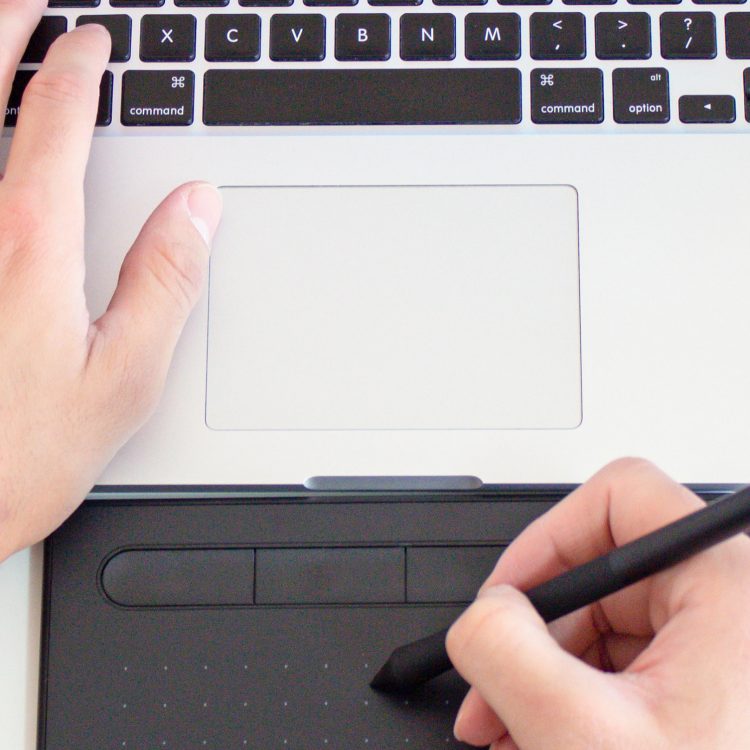Photo of left handing typing on a macbook and right hand drawing using a digital pen