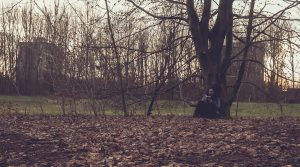 Jack sat against a tree reading a book. There are leaves all over the ground and the sun is setting.