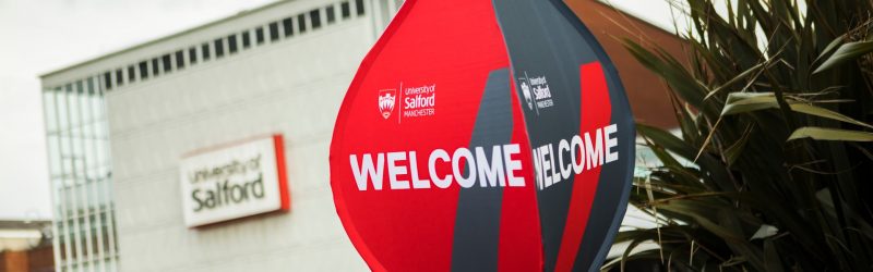 University of Salford welcome balloon sign with University of Salford building sign in the background blurred