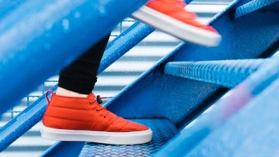 Image of a pair of feet wearing orange trainers walking up blue steps