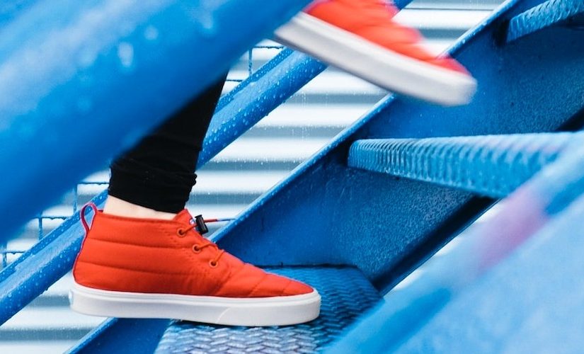 Image of a pair of feet wearing orange trainers walking up blue steps