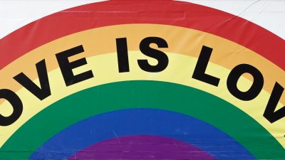 A painting on a a wall of a rainbow with the words "love is love"