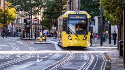 Photo of a yellow tram coming towards the camera on the tram line with people walking on the sidepaths