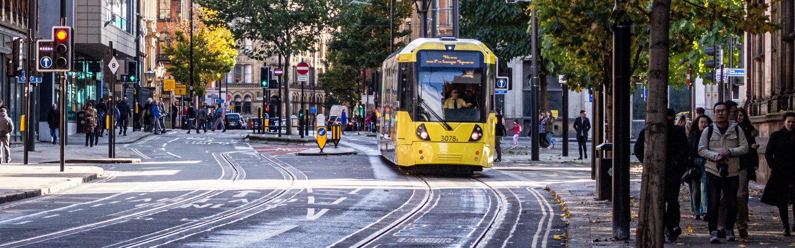 Photo of a yellow tram coming towards the camera on the tram line with people walking on the sidepaths