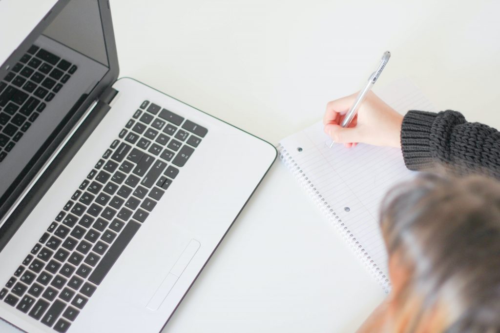 Student writing a study plan next to their laptop