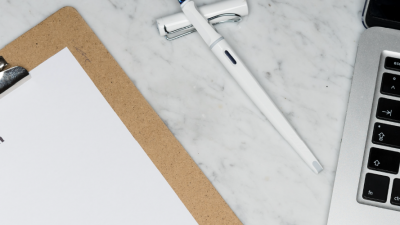 Top down photo of application paper with a laptop on the right and a white pen in-between