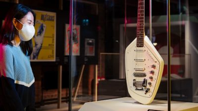 Photo of a women standing infront of a guitar that is placed is a glass box