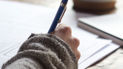 Photo of person writing on paper using a blue pen