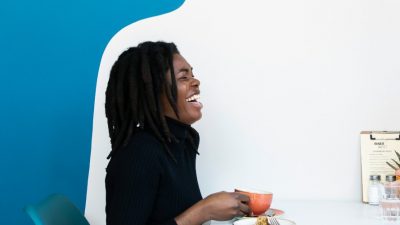 Image of a woman and man against a blue and white background drinking and laughing.