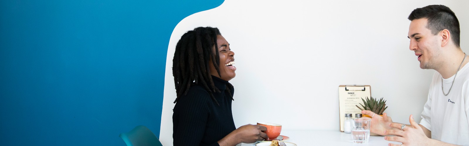 Image of a woman and man against a blue and white background drinking and laughing.