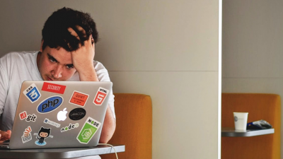 Student holding their head as they complete work on their laptop