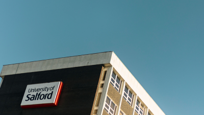 Photo of the top of a University of Salford building against a blue sky