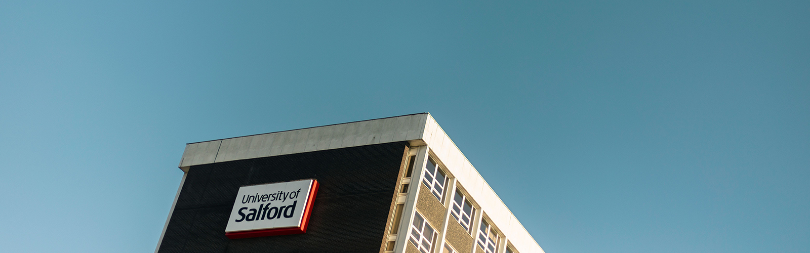 Photo of the top of a University of Salford building against a blue sky