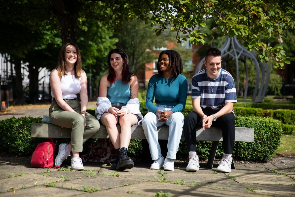 Photo of friends talking to each other sitting on a bench in the garden under the tree