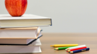 An apple placed on top of a stack of books with colored pencils and alphabet blocks to the right