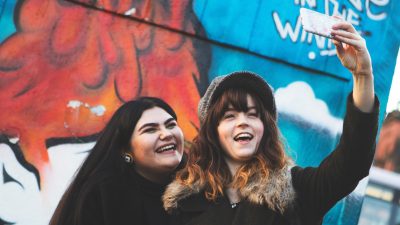 2 people taking a selfie in front of graffiti