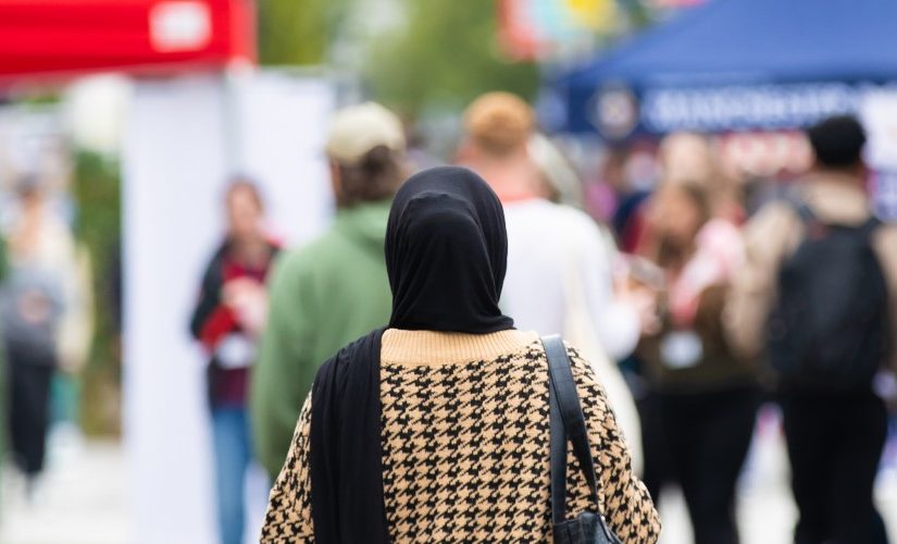 Photograph of Welcome Week at the University of Salford, outside, with a person in a headscarf in the centre of the frame, facing away from the camera. Stalls can be seen in the background.
