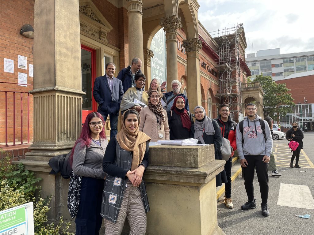 A group of students and staff stand on the steps at the entrance to the Salford Museum