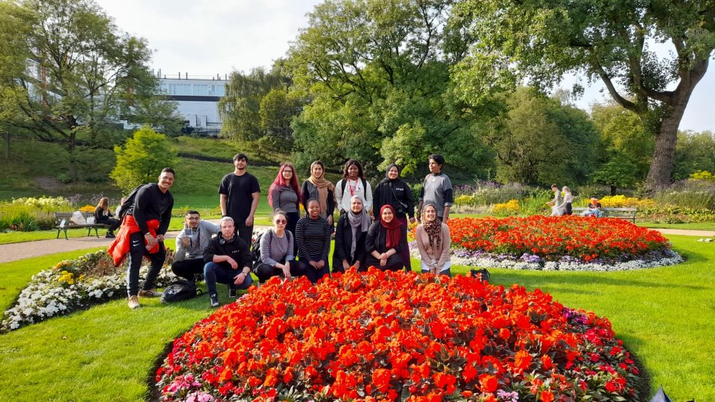A group of students stand pose near some flowers in the park
