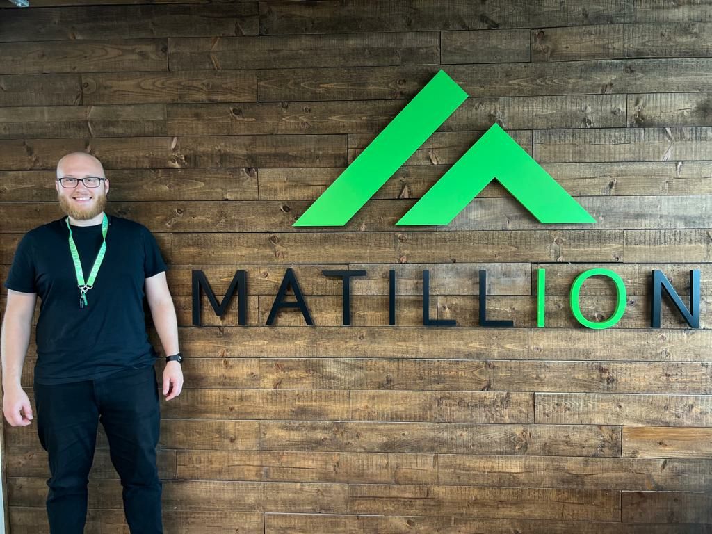 Michal stands next to a Matillion sign and logo on a wall