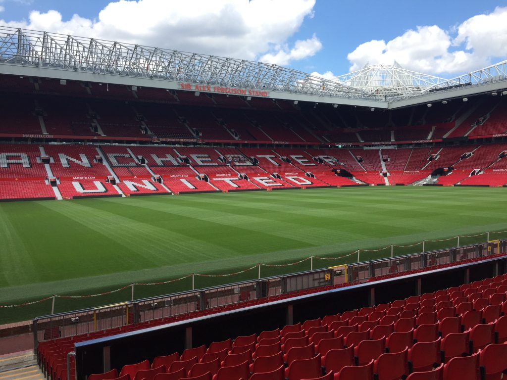 Photo of empty Old Trafford stadium with red chairs, written on the chairs Manchester United. 