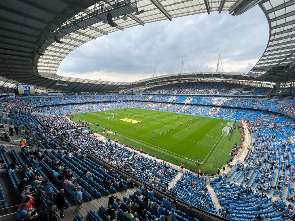 The Etihad stadium with blue chairs during a game of Manchester City team with fans watching the game .