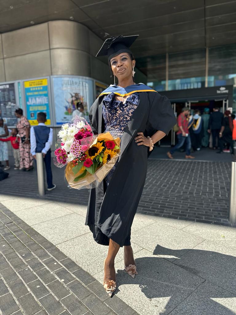 Olubukola in her graduation gown and clutching a bouquet of flowers, stands outside The Lowry theater where her ceremony took place.