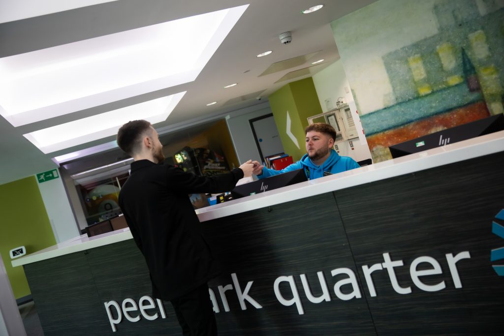 A member of staff at Peel Park Quarter reception gives a keycard to a student.