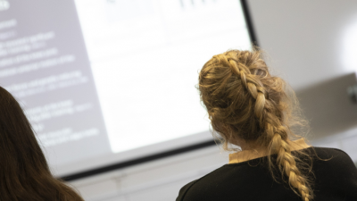 Three students are listening to a presentation and watching a slide show.