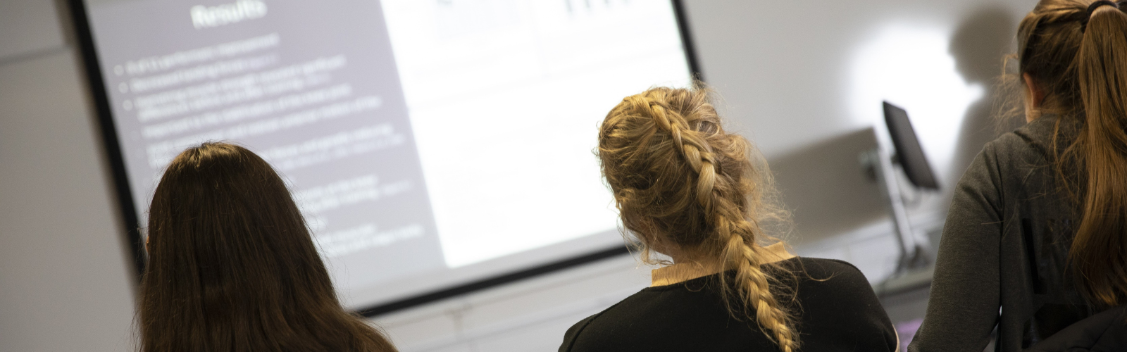 Three students are listening to a presentation and watching a slide show.