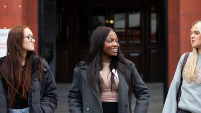 Three students are talking outside the Peel Building.