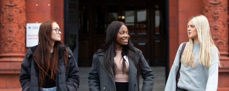 Three students are talking outside the Peel Building.