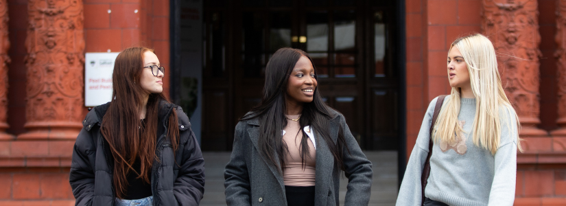 Three students are talking outside the Peel Building.