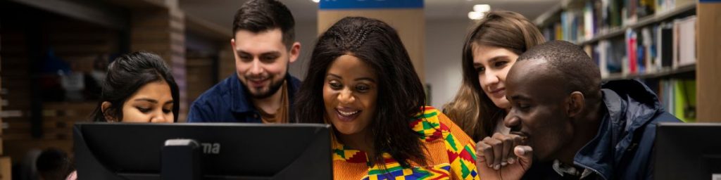 Five people are looking at a computer screen together in the library.