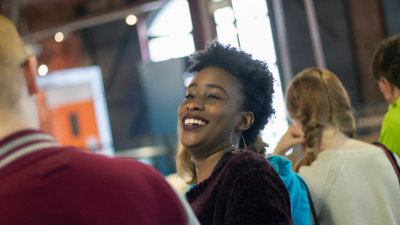 Two students are speaking to each other. One has their back to the camera, while the other is visible and laughing.