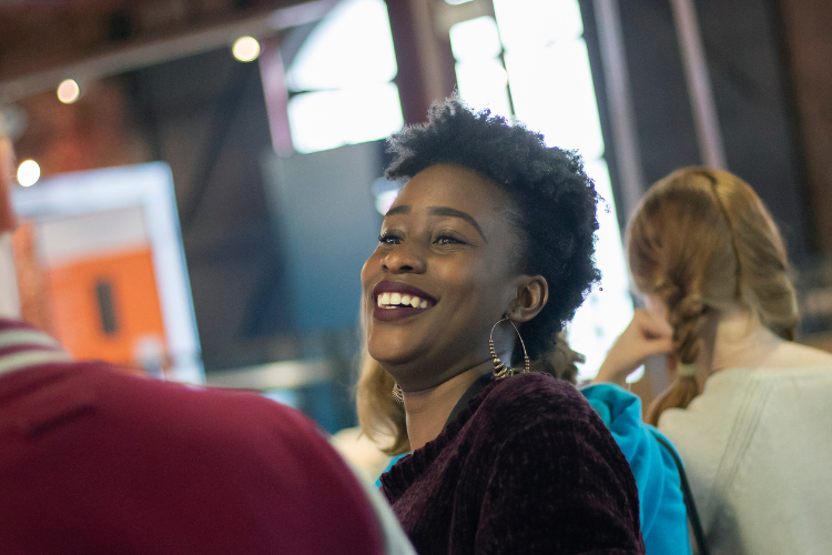 Two students are speaking to each other. One has their back to the camera, while the other is visible and laughing.