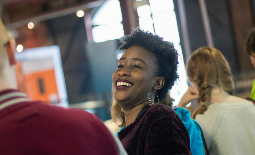 Two students are speaking to each other. One has their back to the camera, while the other is visible and laughing.