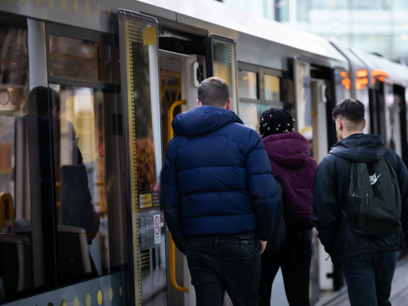 Three three students board a tram at Salford Quays.