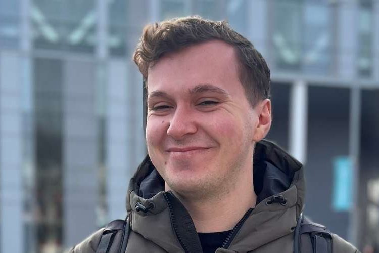 James (a student) standing outside of the New Adelphi building smiling towards the camera.