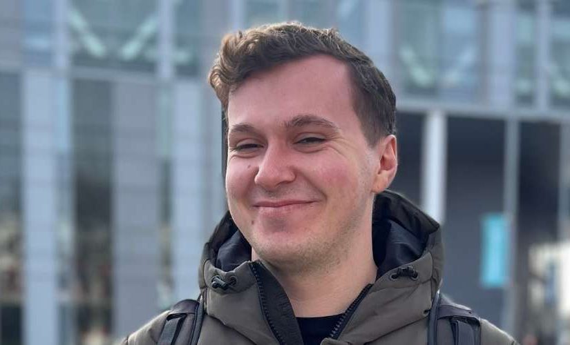 James (a student) standing outside of the New Adelphi building smiling towards the camera.