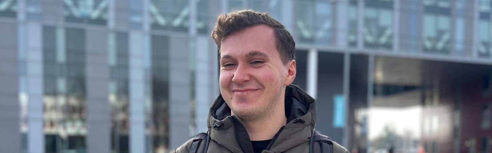 James (a student) standing outside of the New Adelphi building smiling towards the camera.