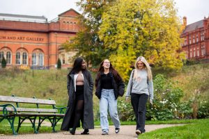 Three students walking through Peel Park on a sunny day.